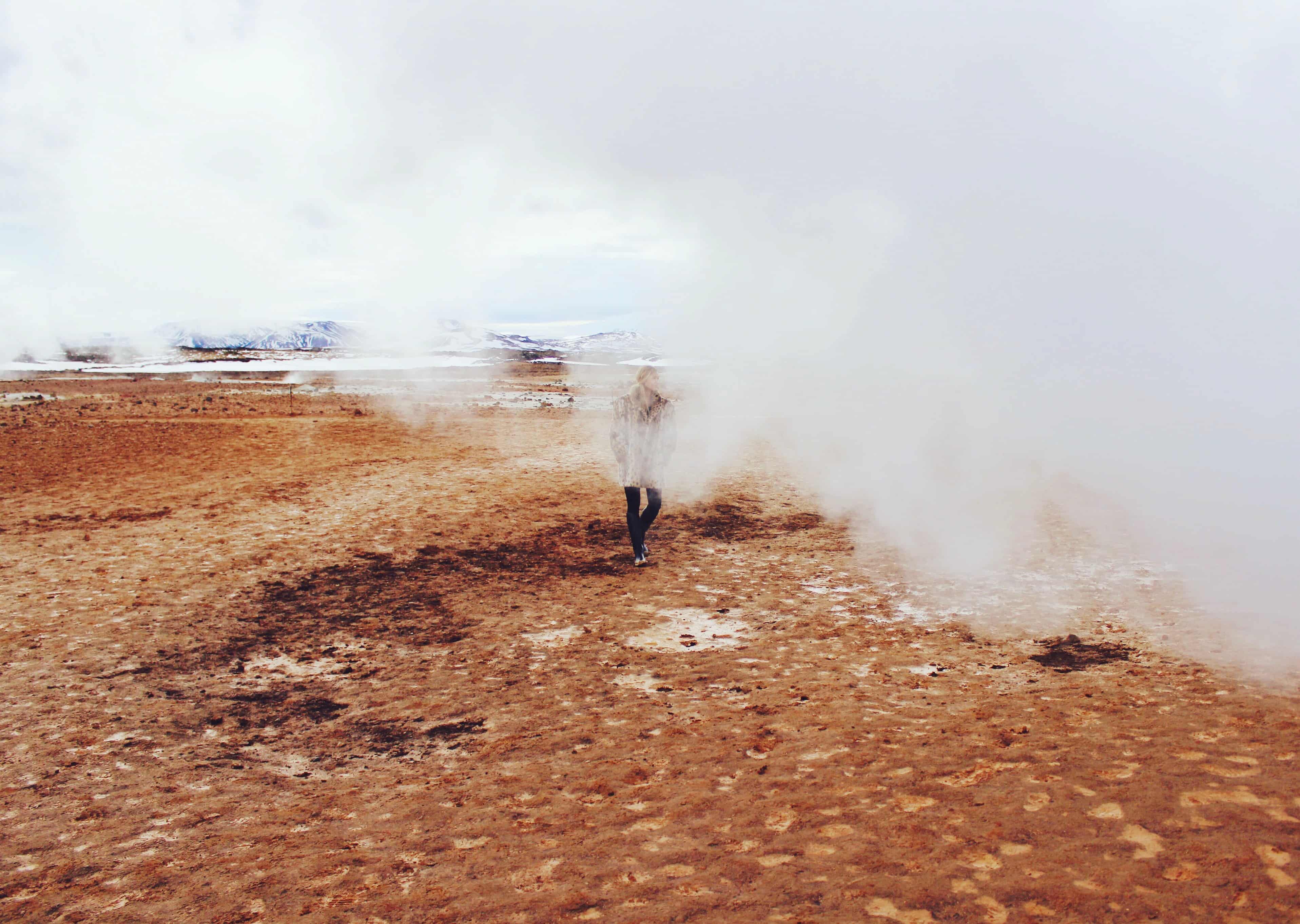 A figure standing amid geothermal steam in an open landscape